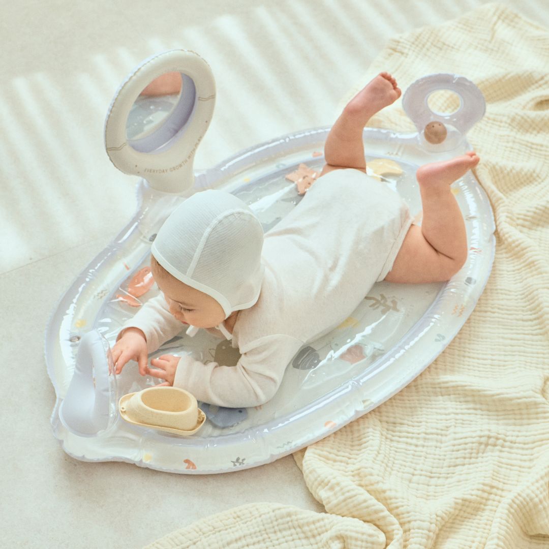 Baby lying on a transparent inflatable play mat with toys on a soft surface